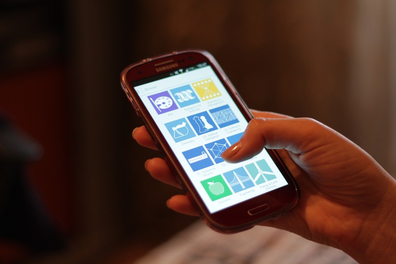 A hand holding a generic smartphone with its home screen visible.