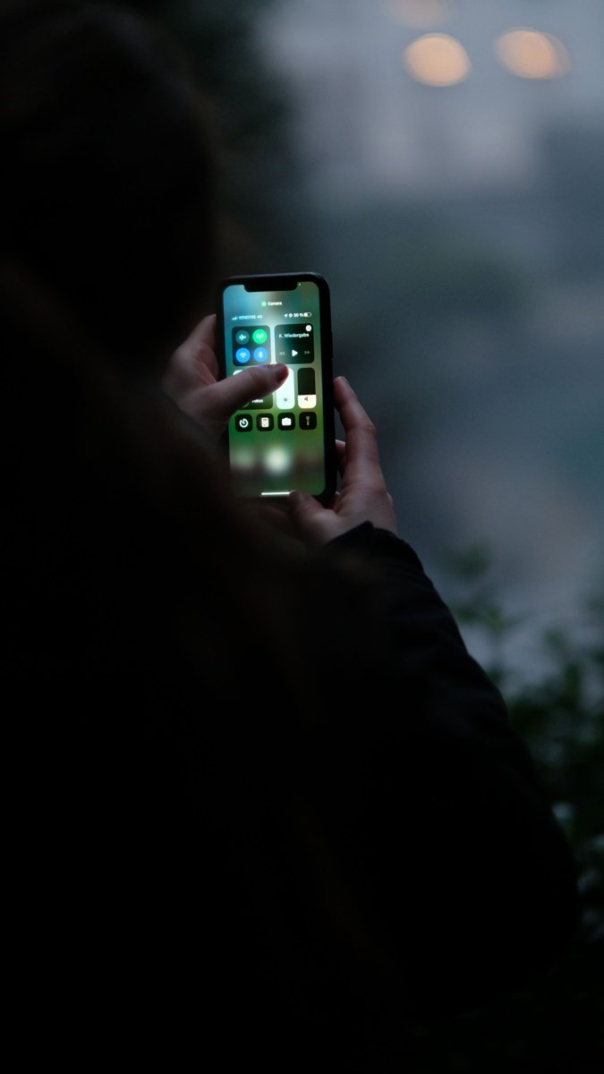 A person holding and checking a smartphone outdoors in low light.
