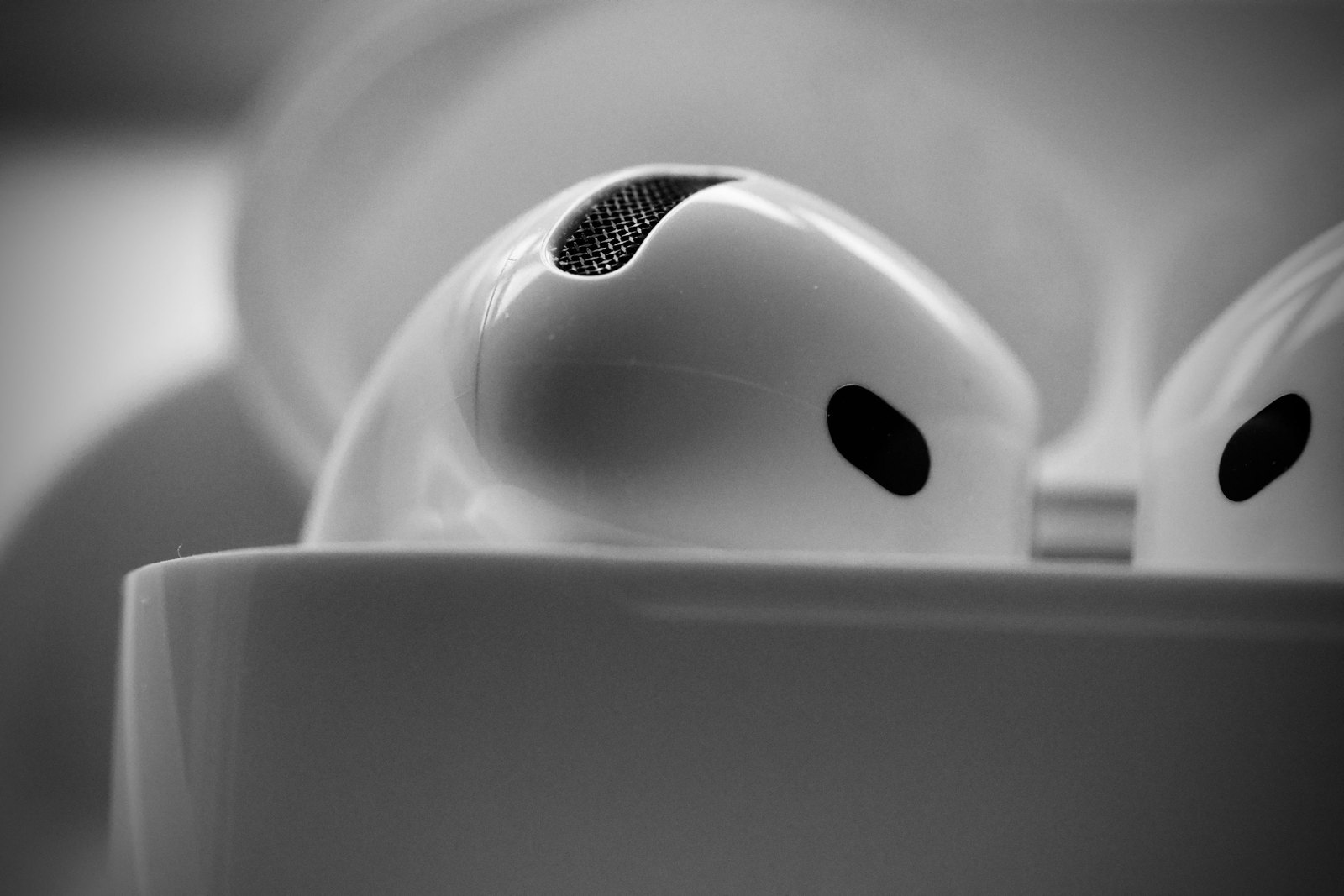 Close-up of white wireless earbuds in a charging case, showing a mesh opening.