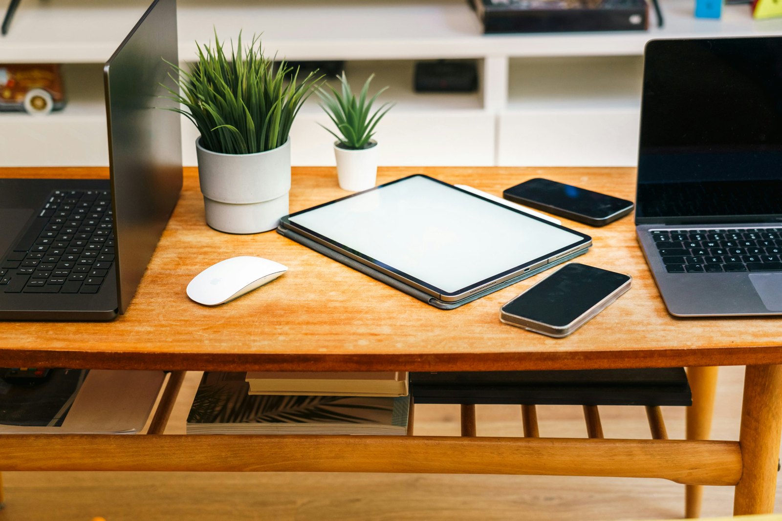 Laptop and tablet on a wooden desk with phones and a wireless mouse