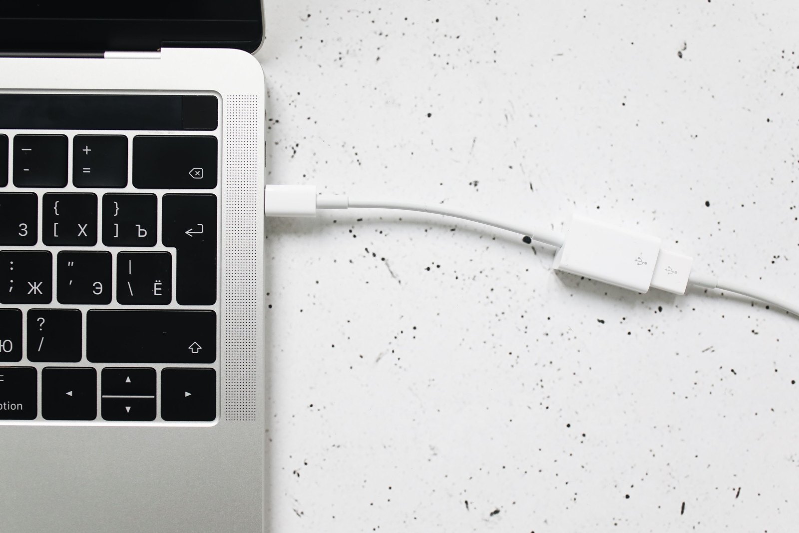 Close-up photograph of a USB cable connected to a laptop keyboard on a white textured surface