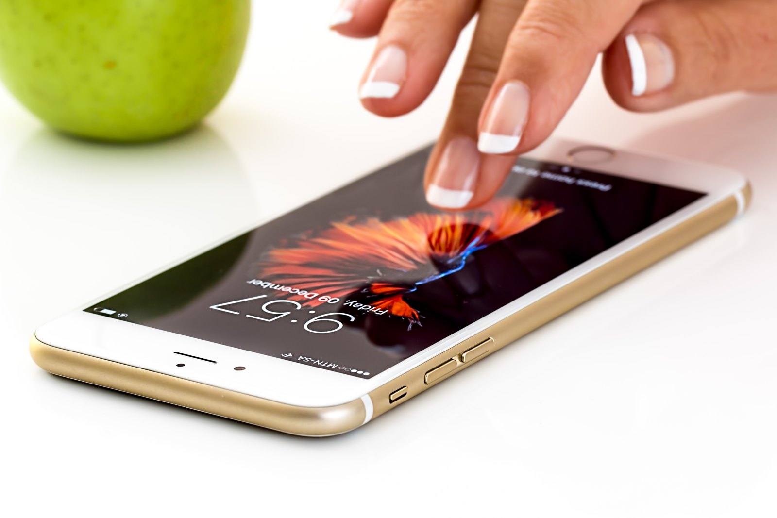 A hand touching a generic gold smartphone on a white surface.